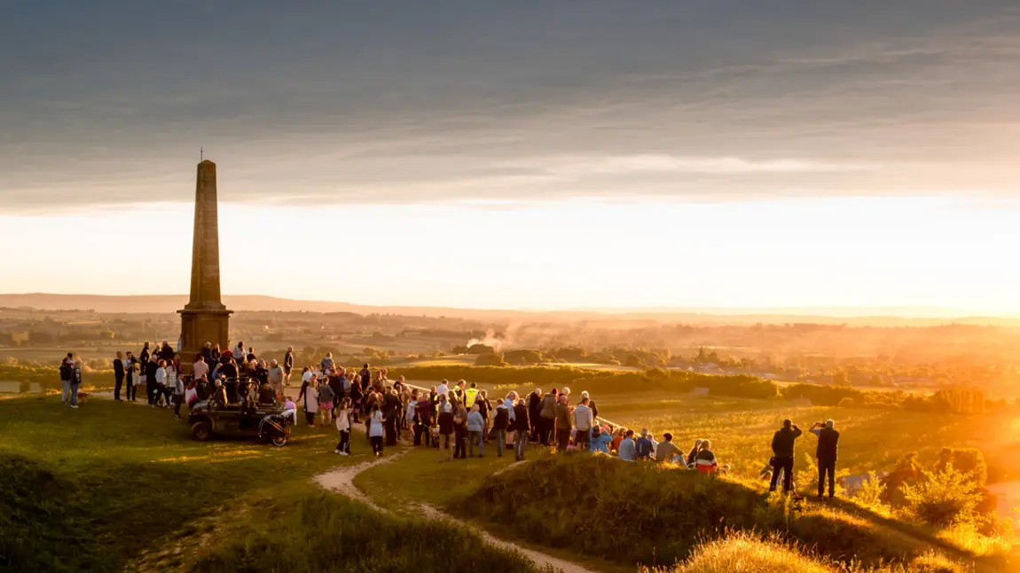 A large group of people stand on top of Ham Hill summit at sunset
