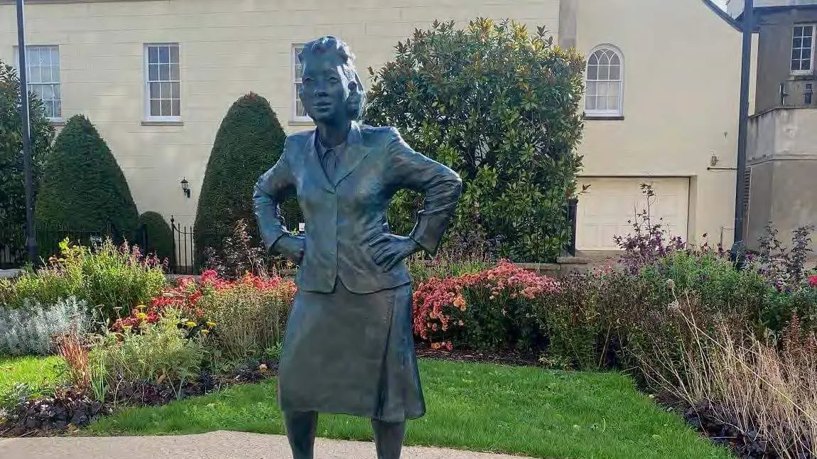 Life-sized statue of a woman in a small, landscaped garden