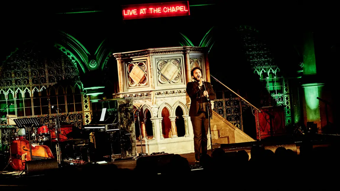 Nish Kumar performing at Union Chapel in front of pulpit and Live at the chapel LED sign Nish Kumar performing at Union Chapel in front of pulpit and Live at the chapel LED sign