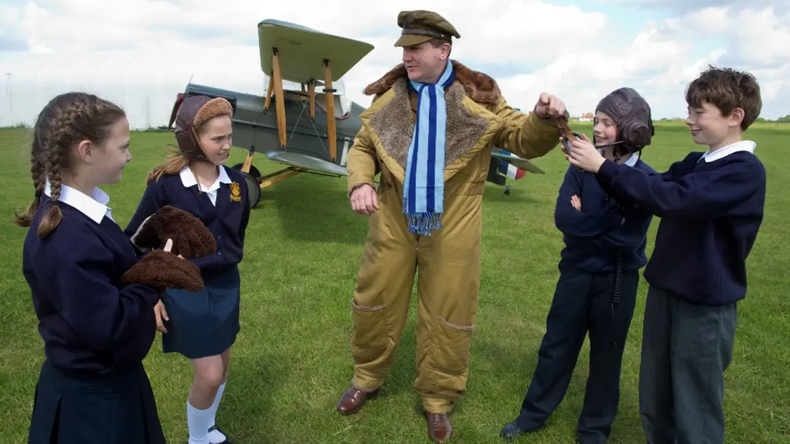 Four children with a man in First World War dress in front of a biplane