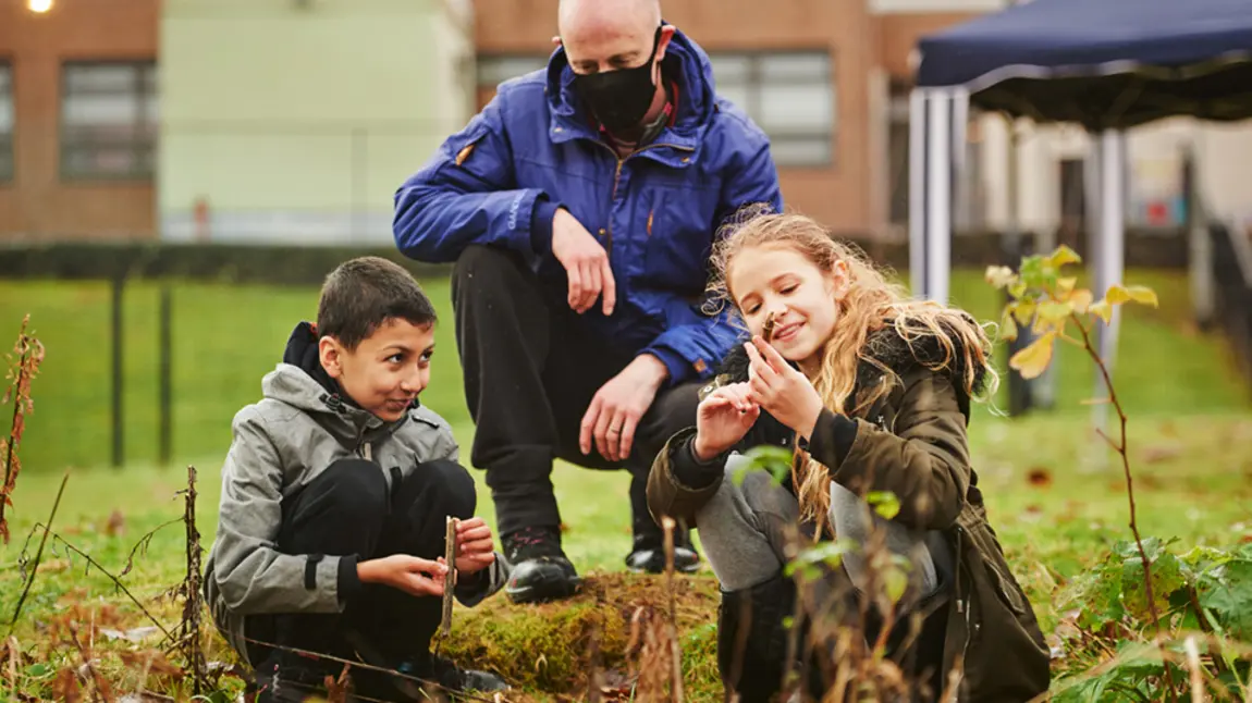 Two school children learning outdoors, watched over by a teacher