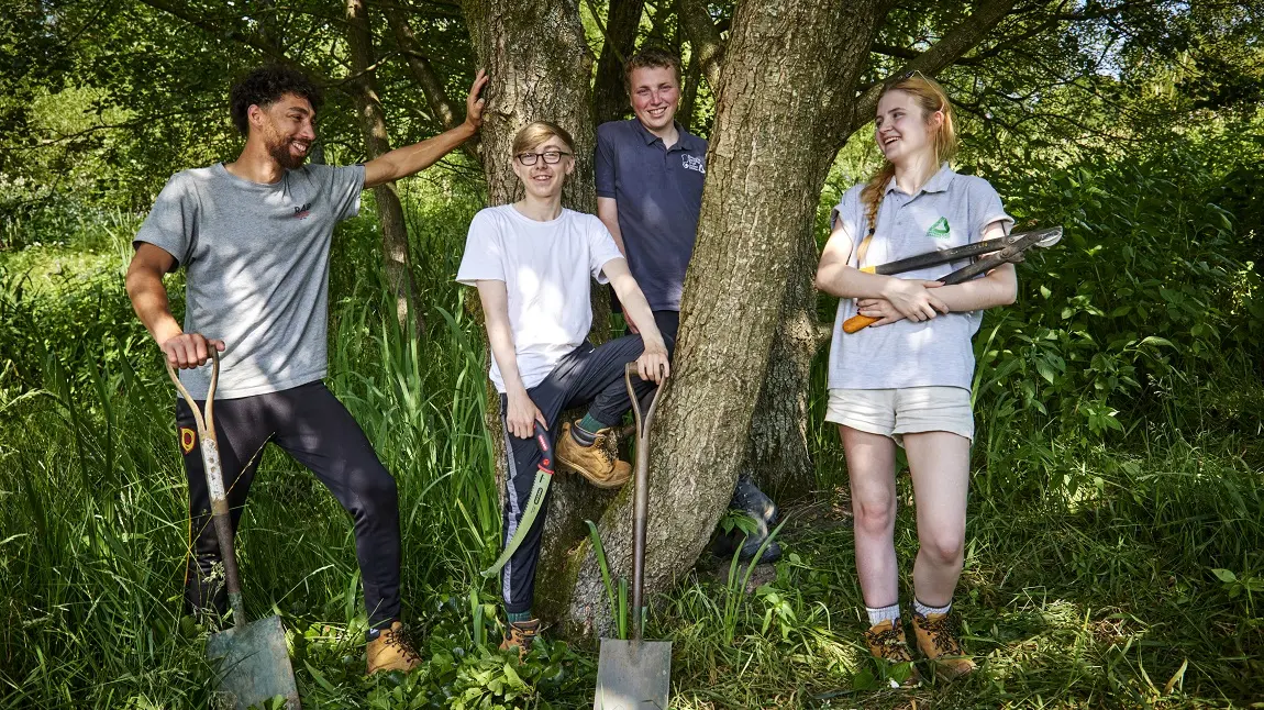 Young people standing in nature with gardening tools