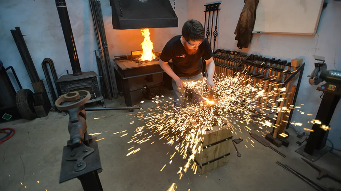 A blacksmith hitting metal, surrounded by a spray of sparks