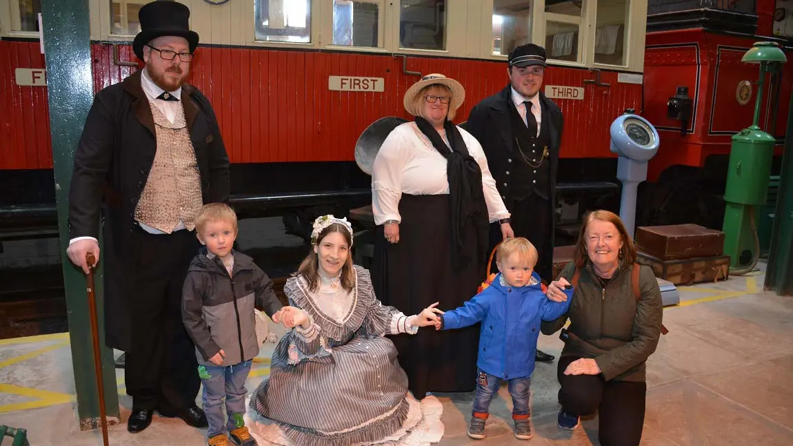 People in period costumes with children in front of an old train