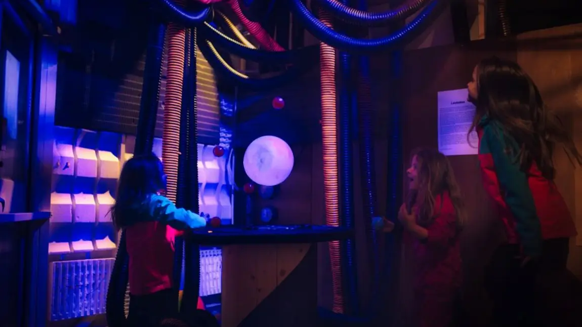 Three children interact with the hovering ball exhibit and balance balls on different air streams