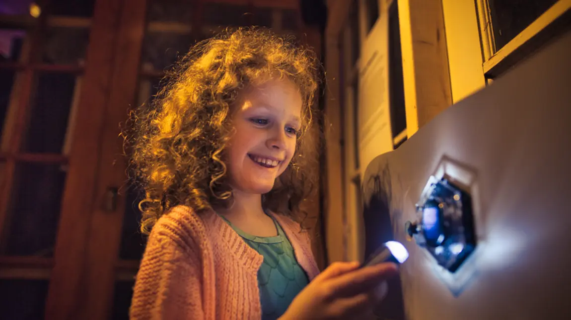 A child interacting with one of the Reimagining Reality exhibits and shining a light onto a shape on the wall.