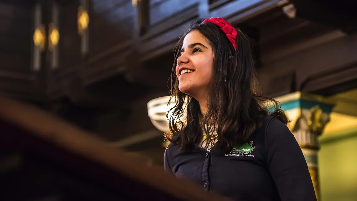  A young child in a school uniform looking up and smiling inside a synagogue 