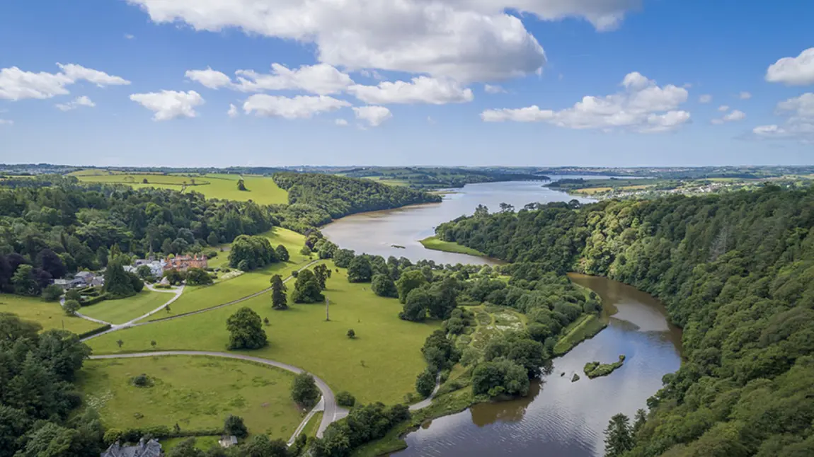 Aerial view over green valley with trees, grass, curving river and blue sky