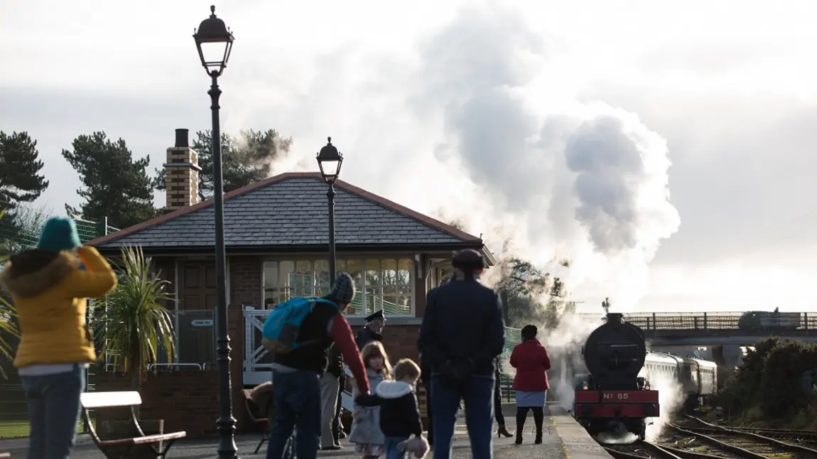 Family gathered on the platform at Whitehead Railway station watching a locomotive approach