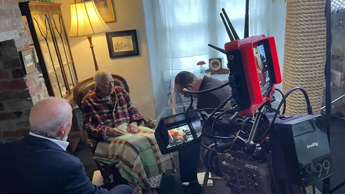 Behind the scenes at a film set: three actors act a scene in a living room while a camera films