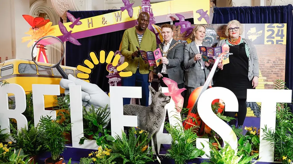 Four people pose with leaflets behind large letters spelling 'Belfast' surrounded by foliage and props