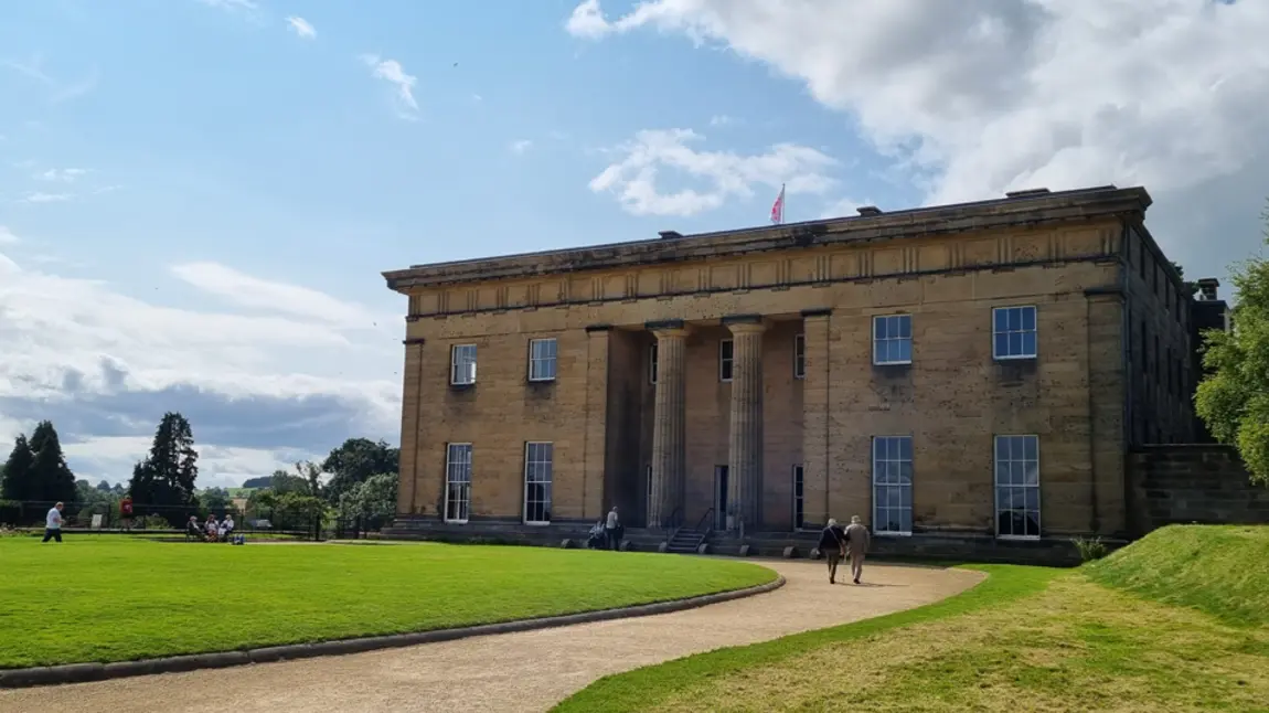 The facade of Belsay Hall on a sunny day, with visitors exploring the grounds