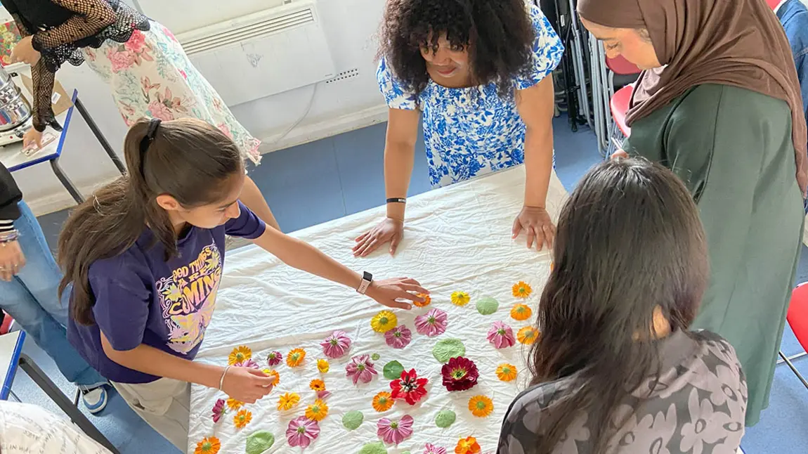 A group of young people arranging flowers and leaves on a white sheet
