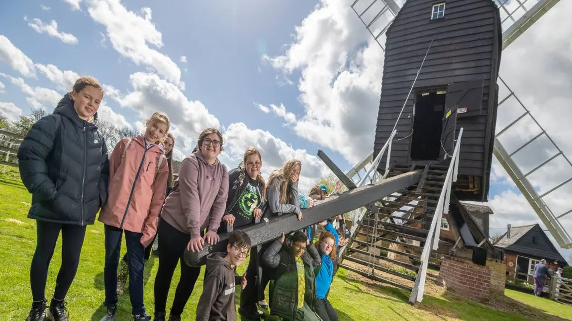 A group of children leading on a piece of wood attached to a windmill.