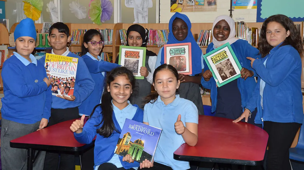 Group of children hold books whilst looking at the camera