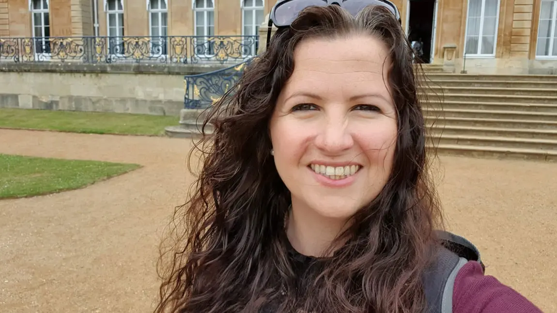 cathryn-evens-1150.jpg Selfie of a women with long dark hair standing in front of a historic house