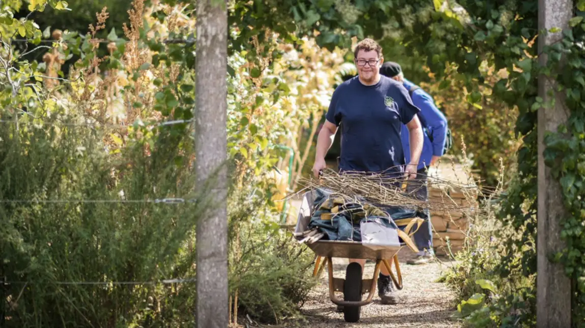 A volunteer with a wheelbarrow of debris, cleaning up the Chelsea Physic Gardens