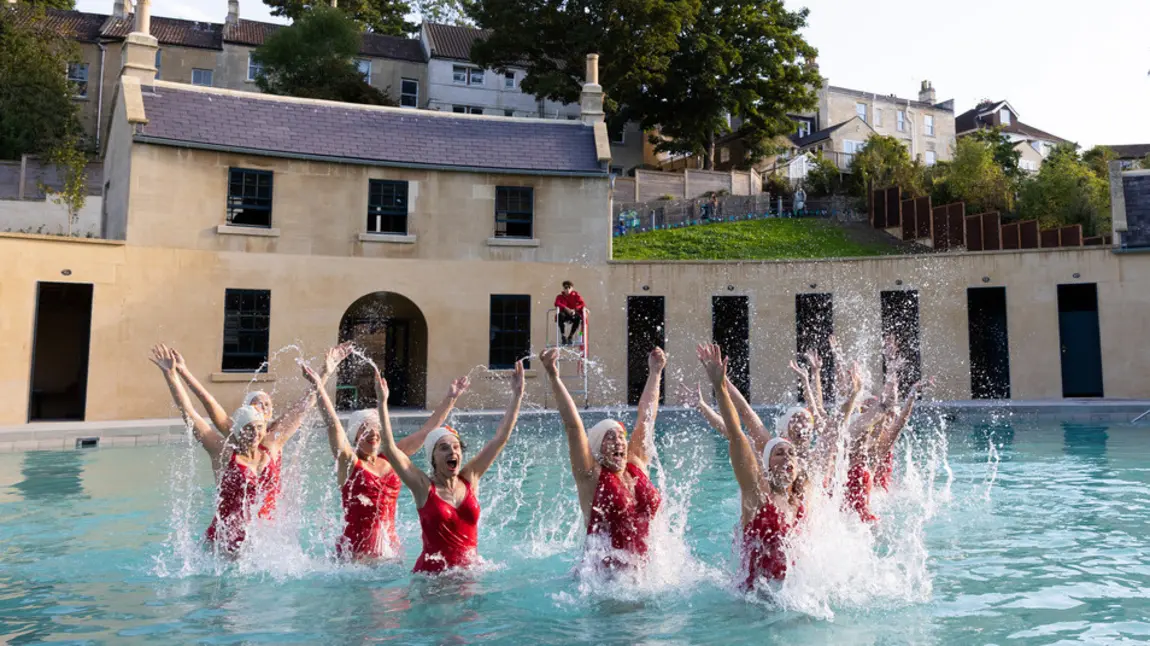 A group of swimmers in red swimsuits jumping out of the water at Cleveland Pools