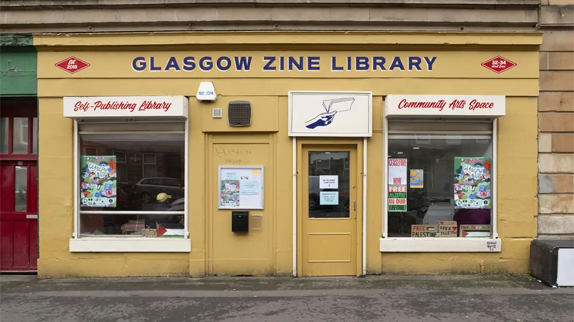 A yellow building on a city street with a writing saying Glasgow Zine Library