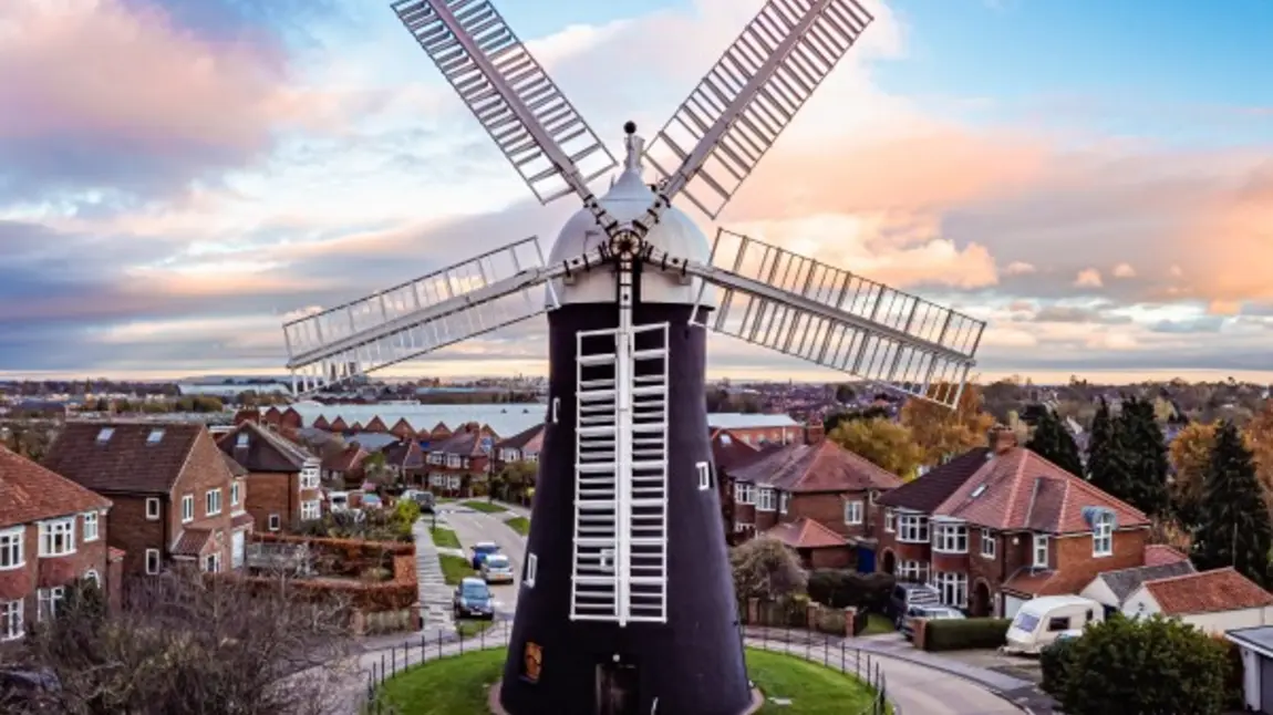 A windmill with houses in the background set against a blue sky