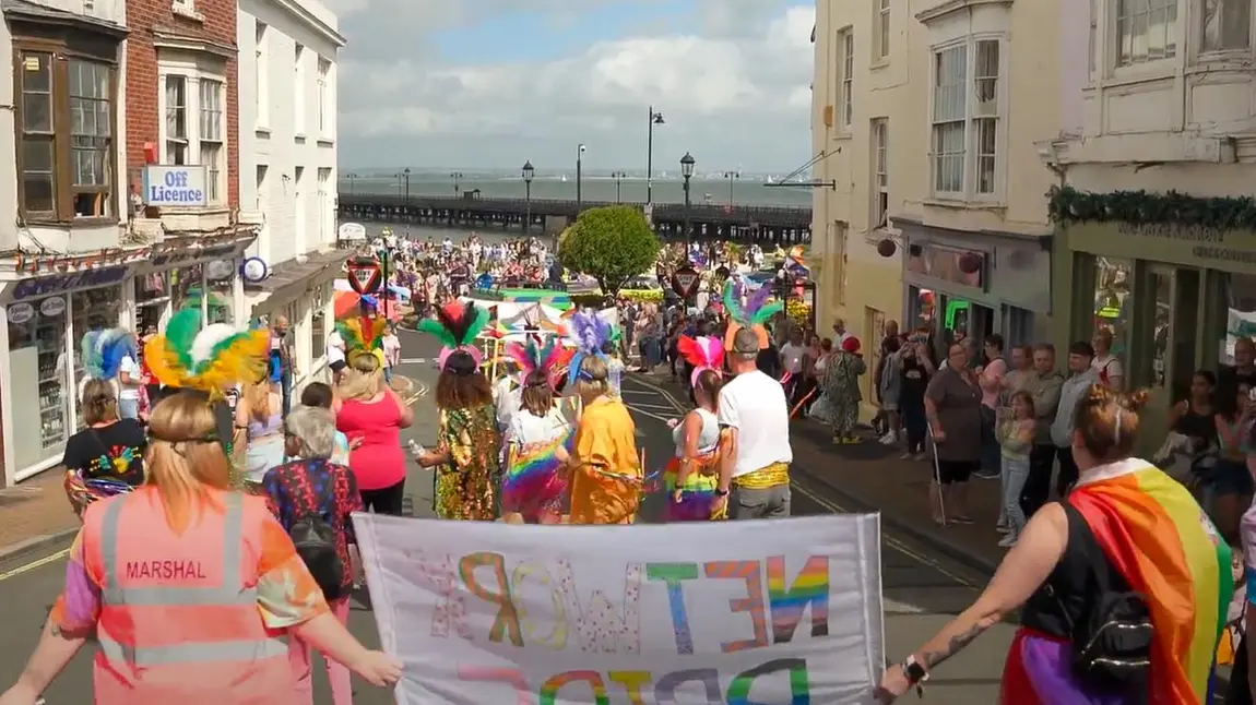 People wear colourful clothes and hold banners and rainbow flags at Isle of Wight Pride.
