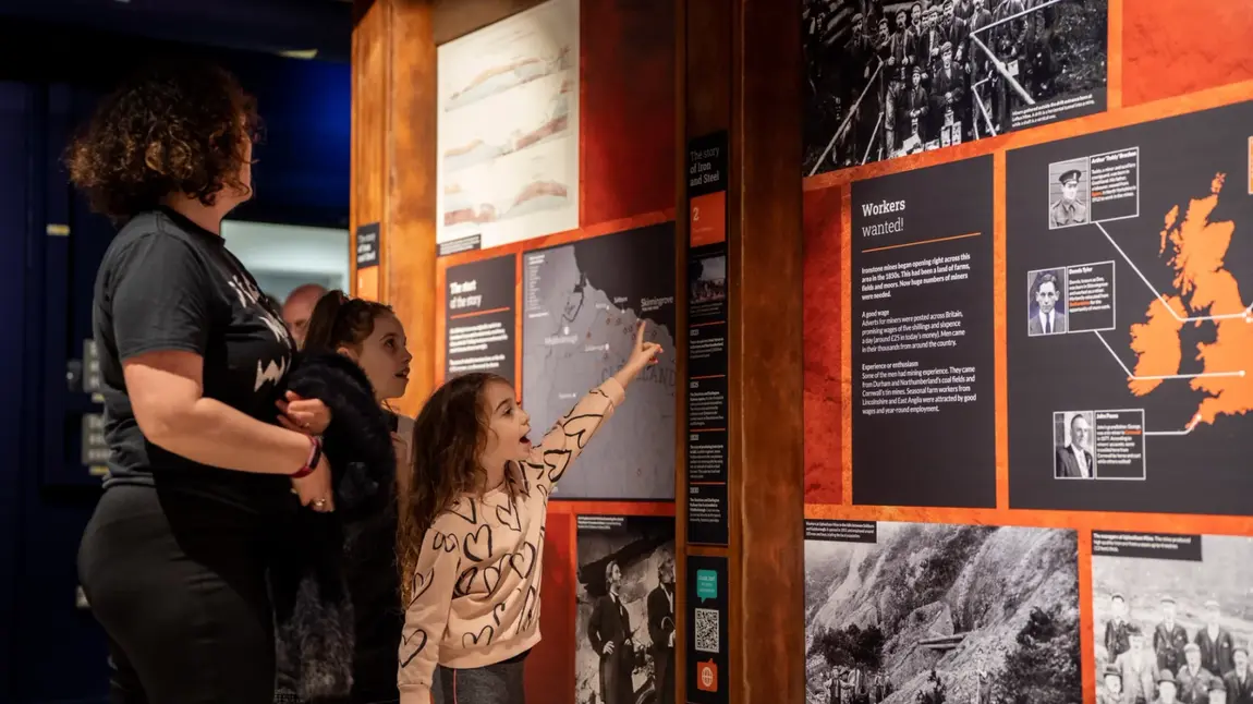 A family looking at an exhibition panel at the Land of Iron that tells the story of iron mining. 