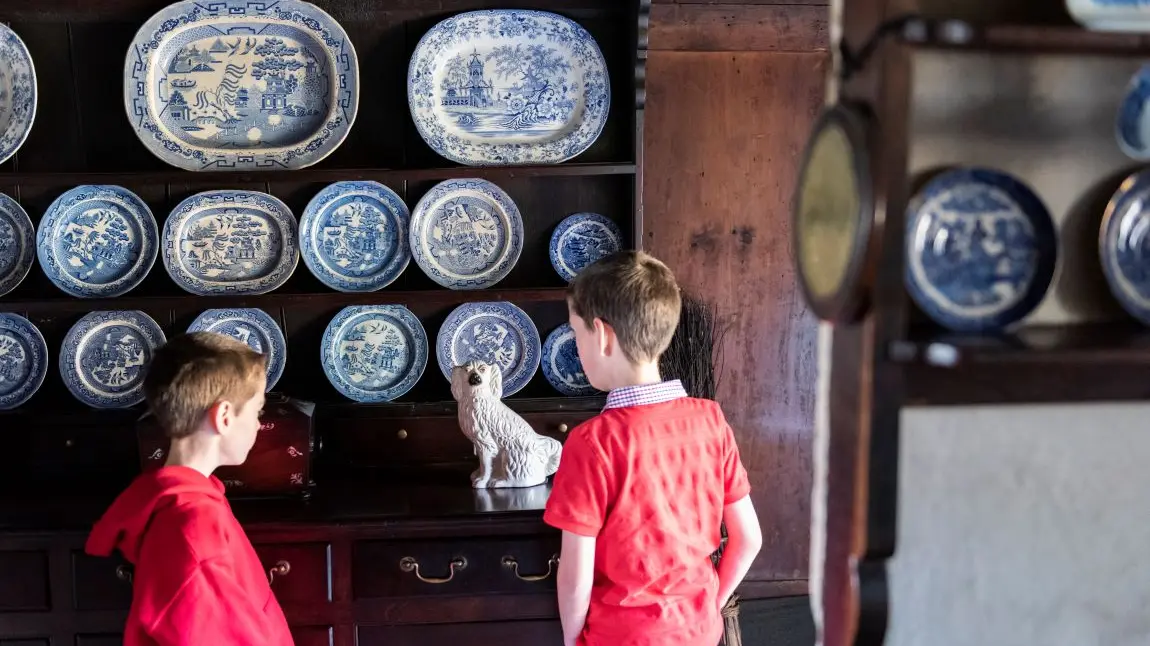 Two children, facing away, looking at a wall of traditional porcelain plates.