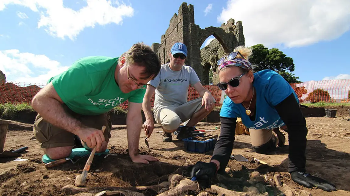 Three people use trowels and brushes to excavate around bones in an archeological dig