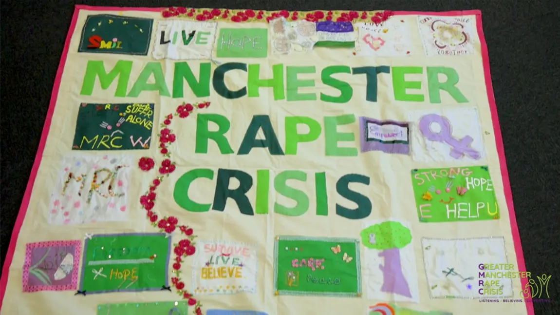 The banner has the words Manchester Rape Crisis in the middle with other phrases and images stitched around it
