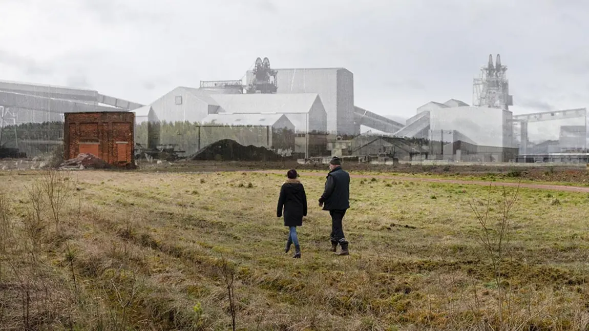 Two people walk across a field. In the background of the photo a historic photo of a colliery has been layered onto the photo