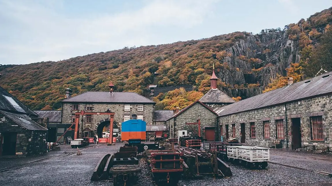 the courtyard of the National Slate Museum in Llanberis, north Wales, with stone factory buildings surrounding a courtyard with industrial equipment for processing slate, and the slate mine visible in the background