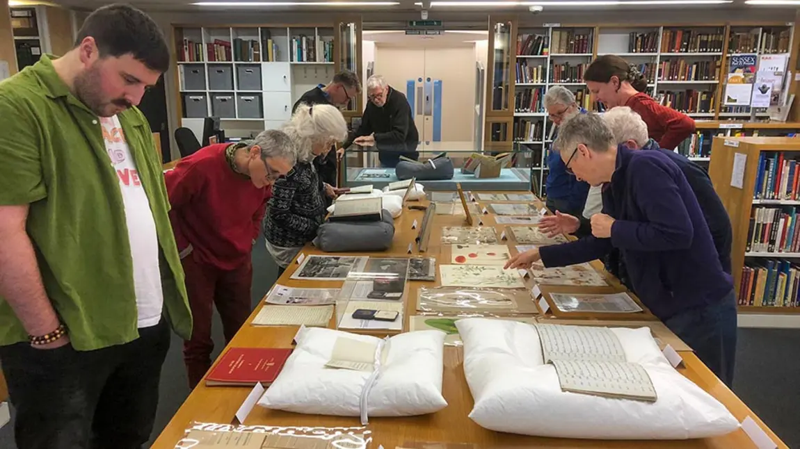 a group of people look at objects from a historical archive laid out on a long table