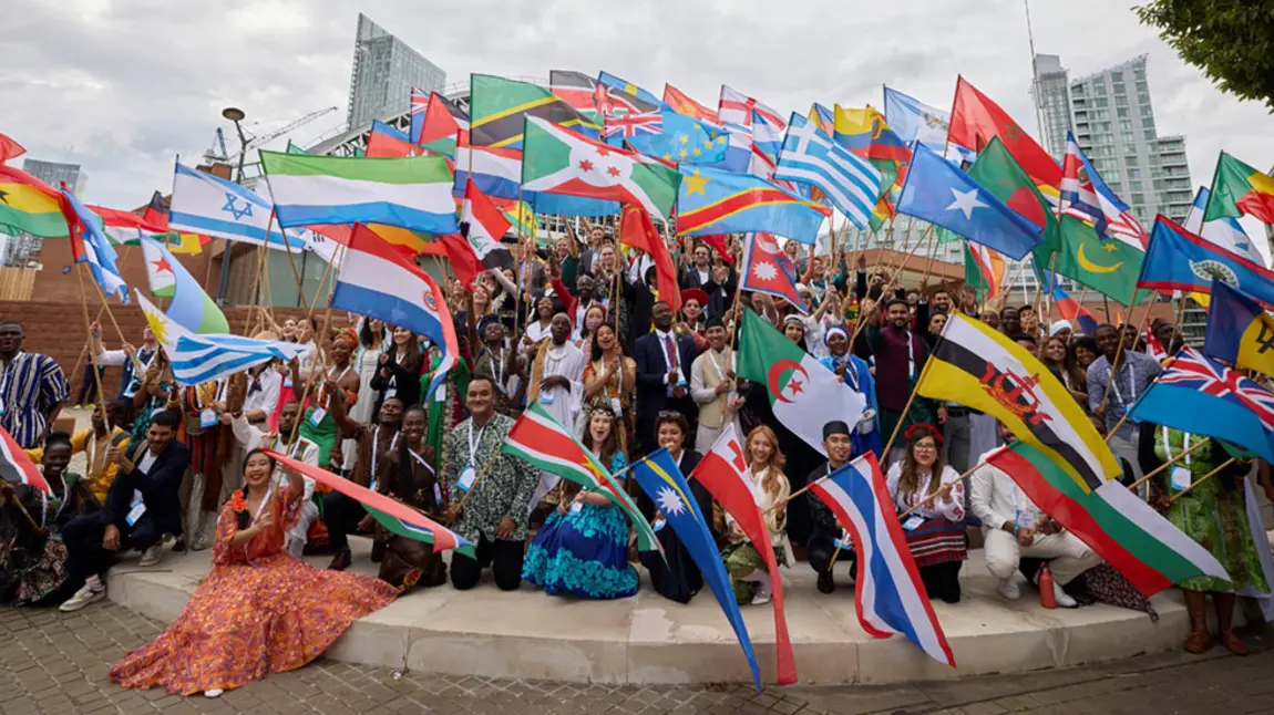 A large group of people sitting on a roundabout all holding flags for different countries of the world