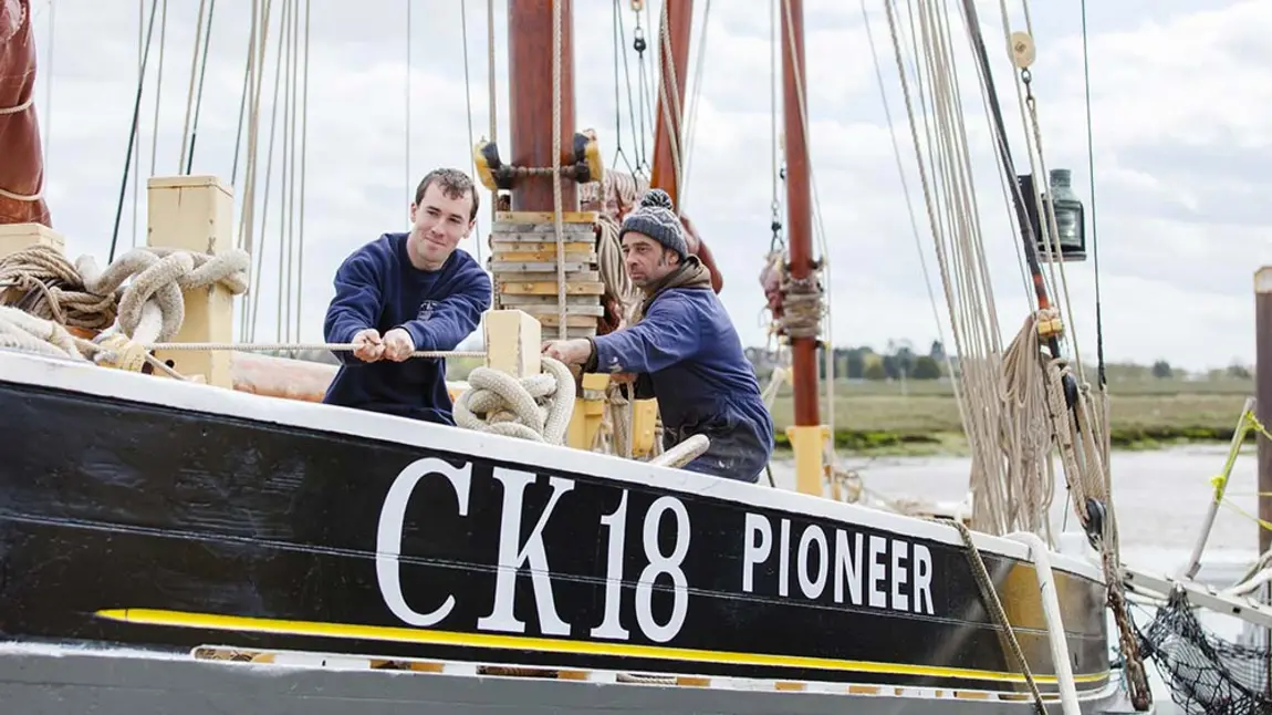 Two people pull a rope on the deck of a historic sailing vessel