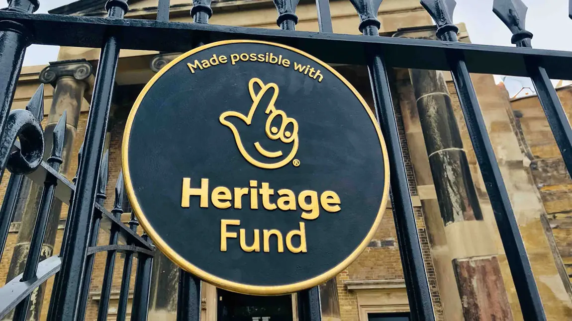 A round plaque of our acknowledgment stamp affixed to an iron fence. A building can be seen in the background.