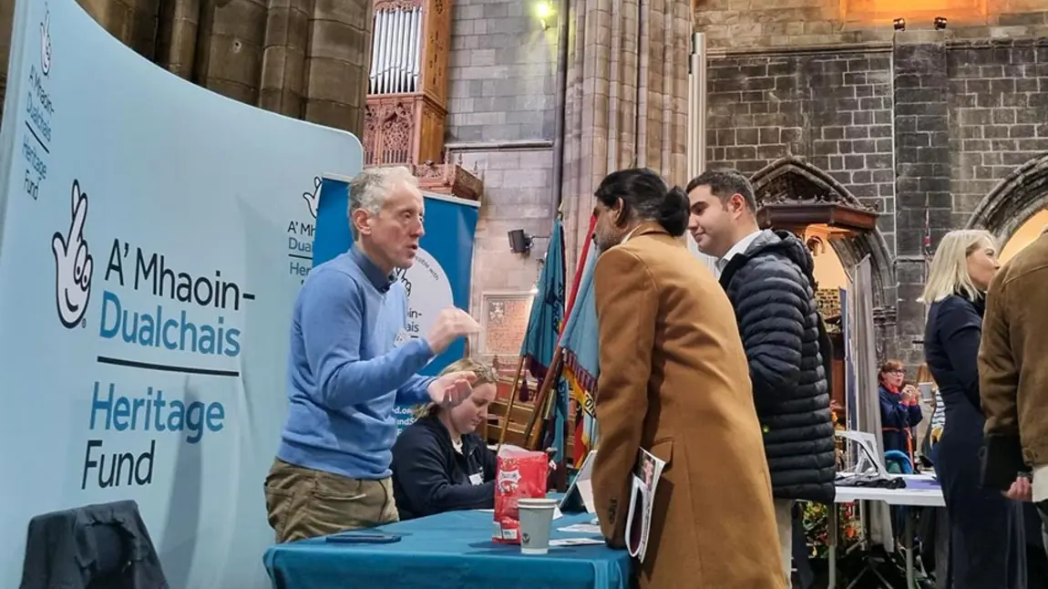 A Heritage Fund member of staff talks with two people at a stall inside a large church
