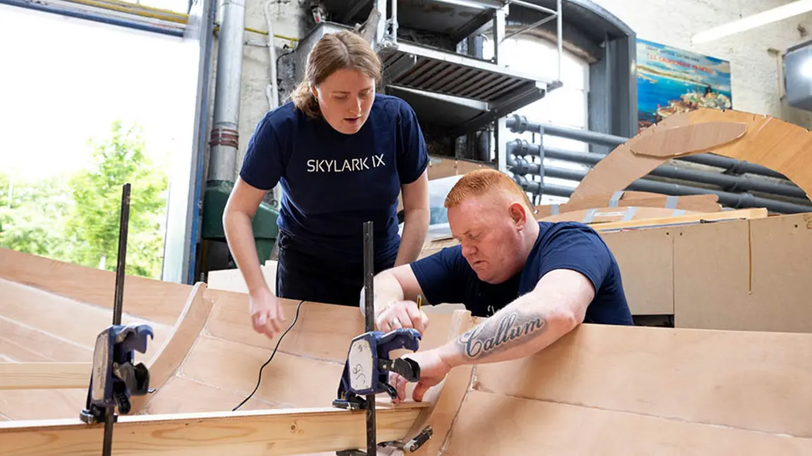Two Skylark IX volunteers work on building a wooden rowing boat 