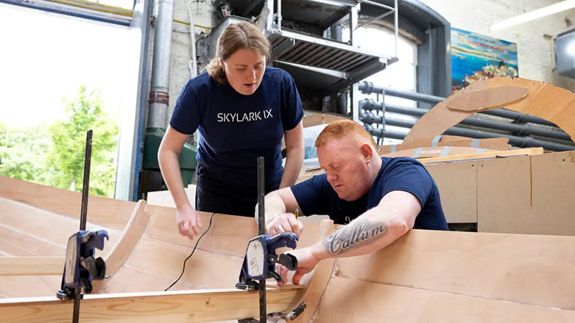Two Skylark IX volunteers work on building a wooden rowing boat