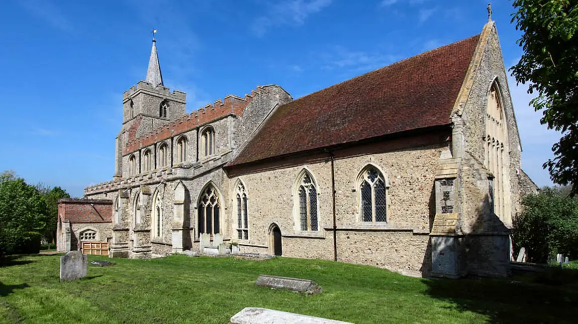 The outside of a stone English parish church with a graveyard in the foreground