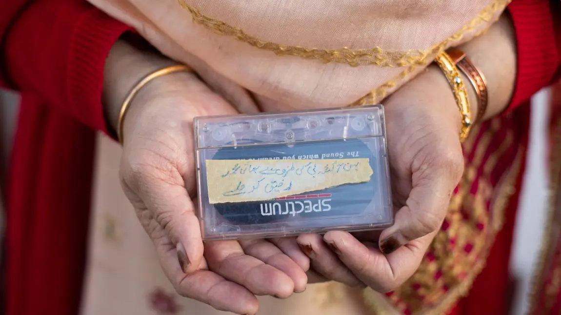 A woman's hands holding a cassette tape. She has bangles on her wrists and is wearing a red cardigan.