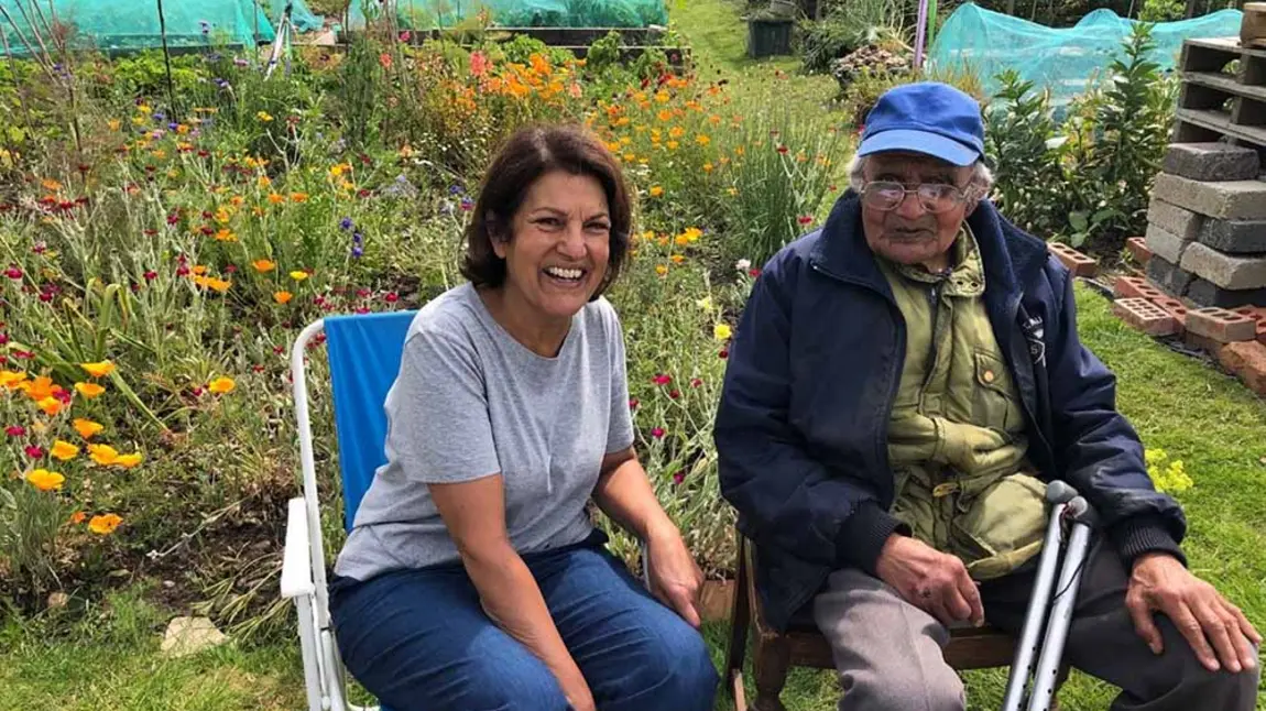 Two people smiling and sitting on camping chairs on an allotment