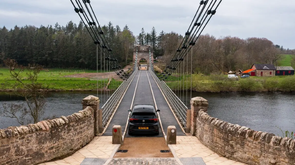 A car crosses the Union Chain Bridge, a small restored suspension bridge over a river.