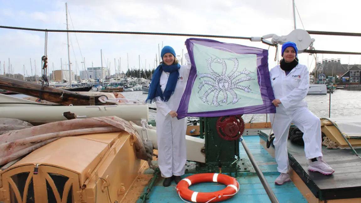 Photograph of two women holding up a flag while standing on a boat.