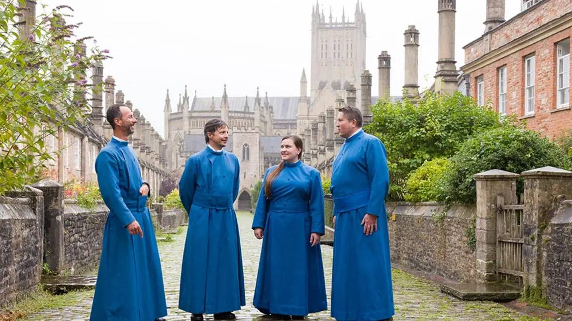 Members of Wells Cathedral’s Vicars’ Choral wear long blue robes and stand outside their medieval stone and brick homes on Vicars’ Close in Wells
