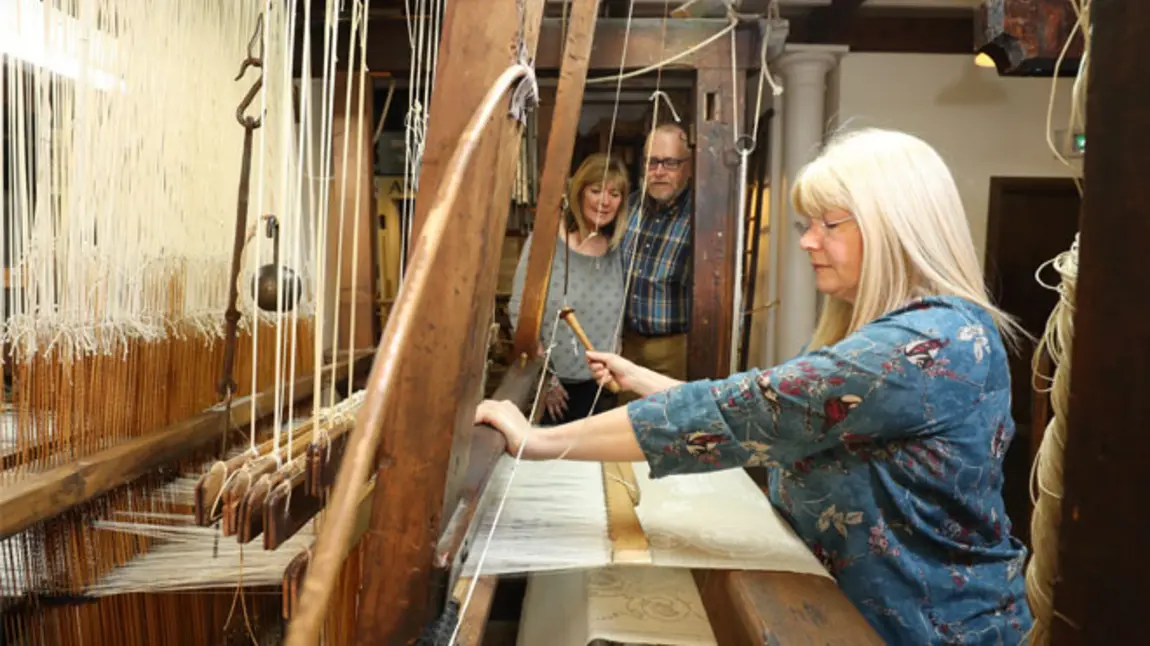 Irish linen damask handloom A person weaves cream coloured fabric on a wooden handloom