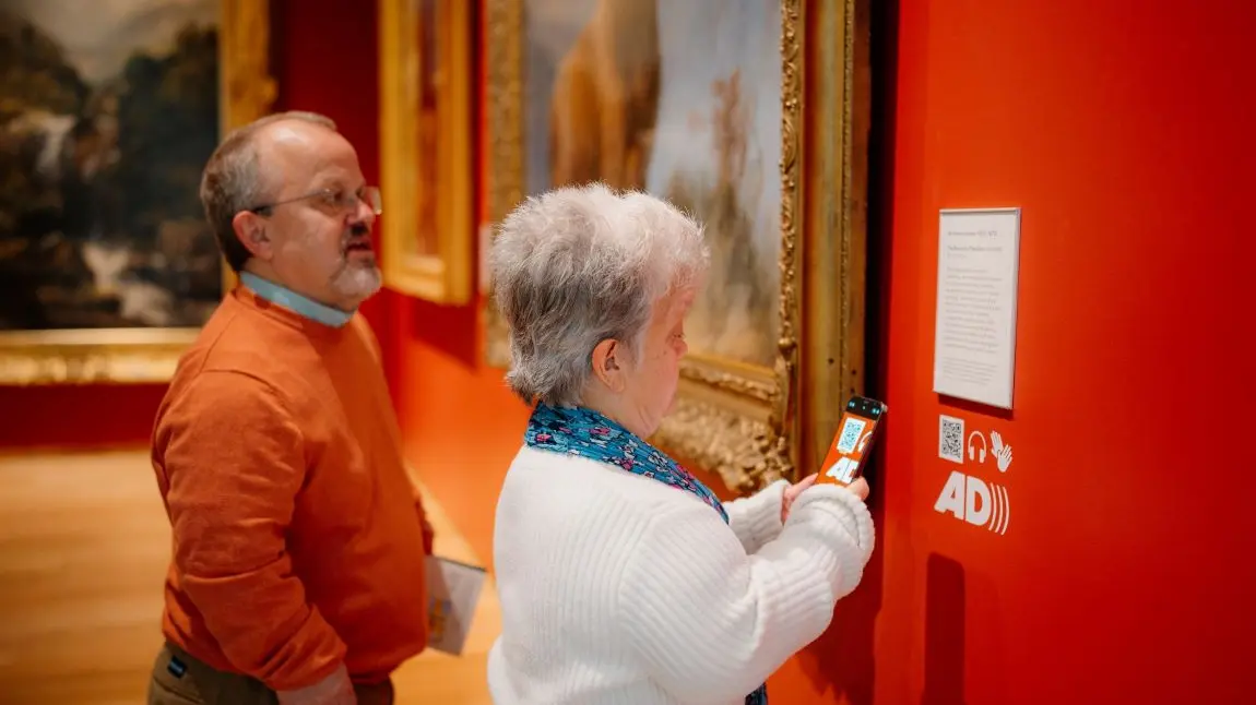 Visitors access audio guides and further resources with their smartphone. Two visitors use a smart phone to scan a QR code that unlocks additional interpretation and audio guides about the Scottish national collection.