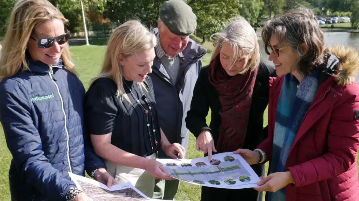 Five people in a park looking at plans on A3 size paper