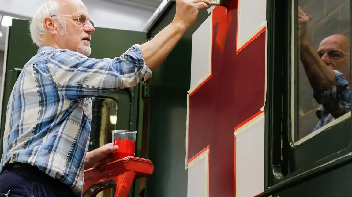 Expert painter Adrian Ashby carefully applies a red cross emblem to the side of a 1907 railway carriage