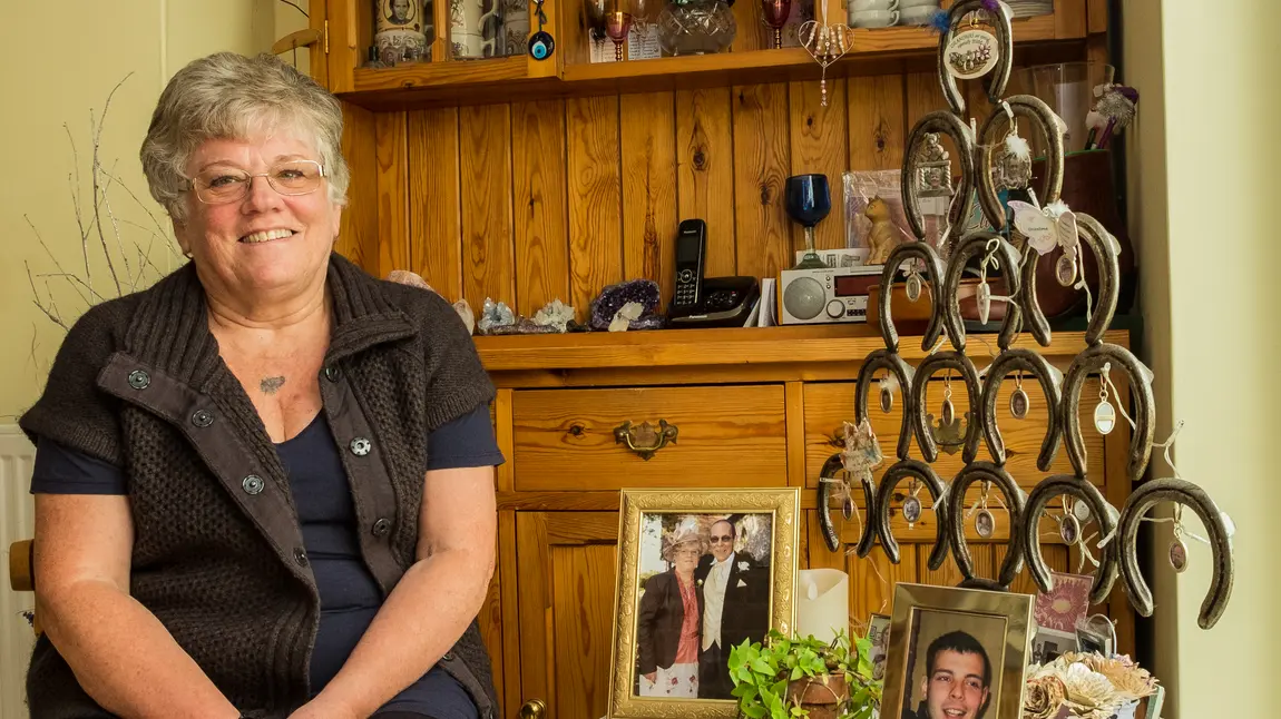 Angela sits in her home, with photos of her late husband and grandson