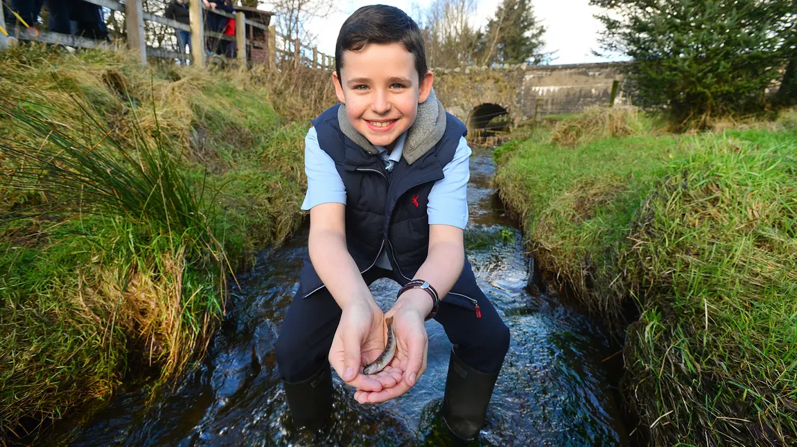 A boy holds a fish in the Ballinderry River